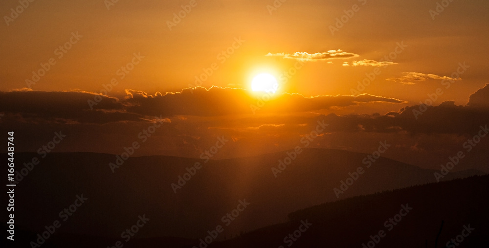 sunset in mountains with hills, colorful sky, sun eith sunlights and clouds