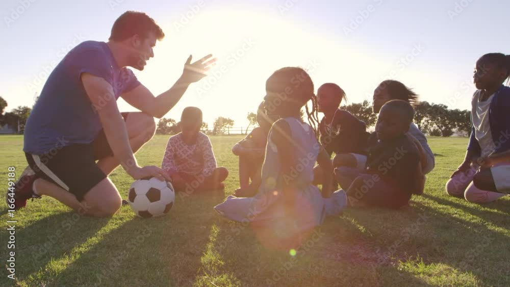 Young school kids and teacher sitting with ball in field