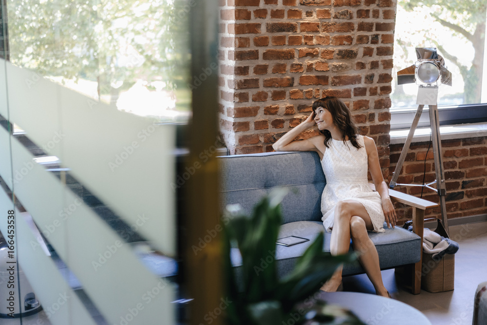 Businesswoman sitting on couch in office, smiling Businesswoman sitting on couch in office, smiling