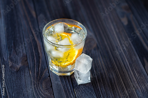 Lemonade with ice cubes and slice of orange in a glass on dark wooden table photo