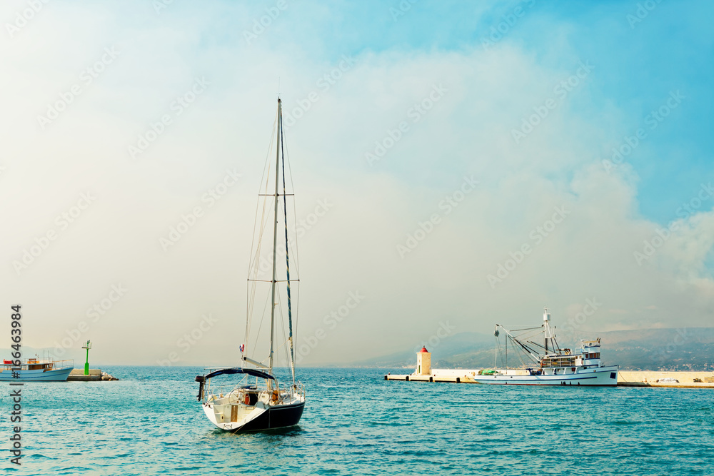 Obraz premium Moored yacht and a fishing trawler in the harbor of a small town called Postira - Croatia, island Brac