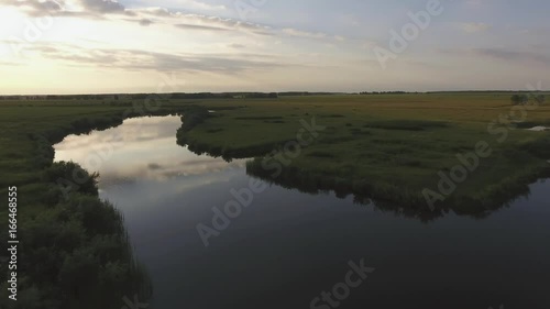 An inspiring natural landscape is a river at sunset, a narrow island with greens in the middle. Sunset sky is reflected in water surface of the river, the river bed. Countryside: silence, nature. photo