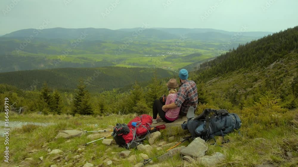 Two hikers: hiking couple sitting together and enjoying the view on the highland landscape, czechia, czech republic Two hikers: hiking couple sitting together and enjoying the view on the highland landscape, czechia, czech republic