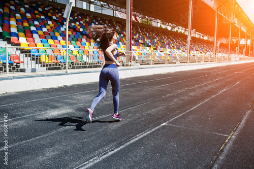 Portrait of a strong fit girl in sportswear running in the stadium.