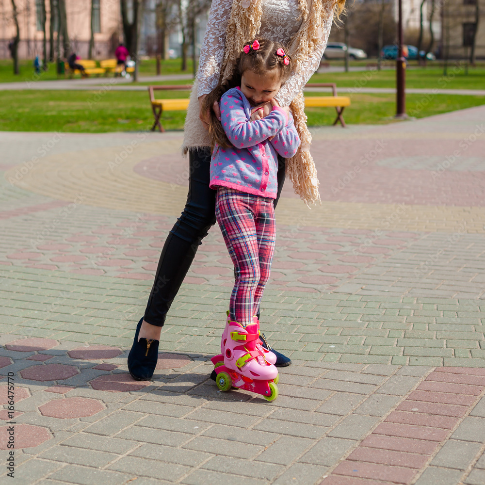 Mom and daughter ride on roller skates. Girl learning to roller skate