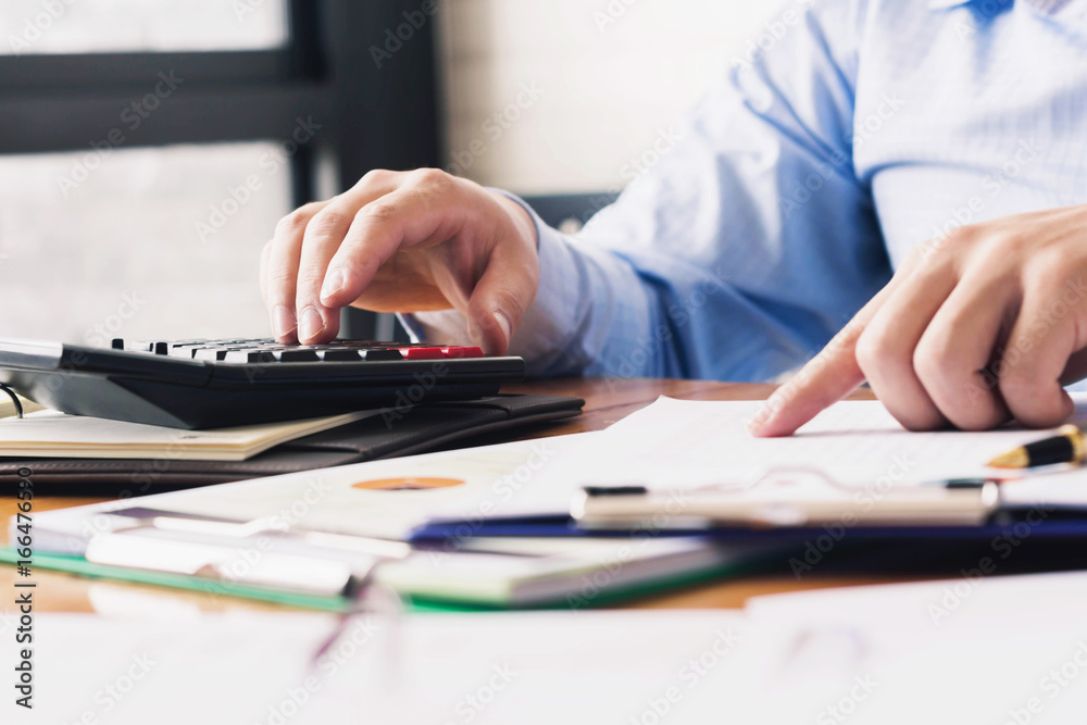 Businessmen working on office desks with calculators, papers, pens and laptops in business, finance and banking concepts. Businessmen working on office desks with calculators, papers, pens and laptops in business, finance and banking concepts.