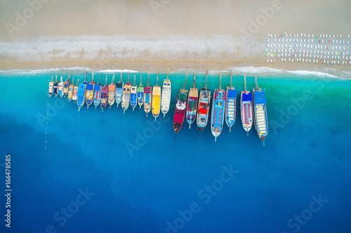 Fototapeta Naklejka Na Ścianę i Meble -  Aerial view of colorful boats in mediterranean sea in Oludeniz, Turkey. Beautiful summer seascape with ships, clear azure water and sandy beach in sunny day. Top view of yachts from flying drone