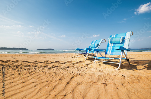 Two blue chaise-longues are on the sand ocean beach