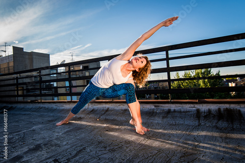 Fit mature woman doing yoga in sunset, urban landscape