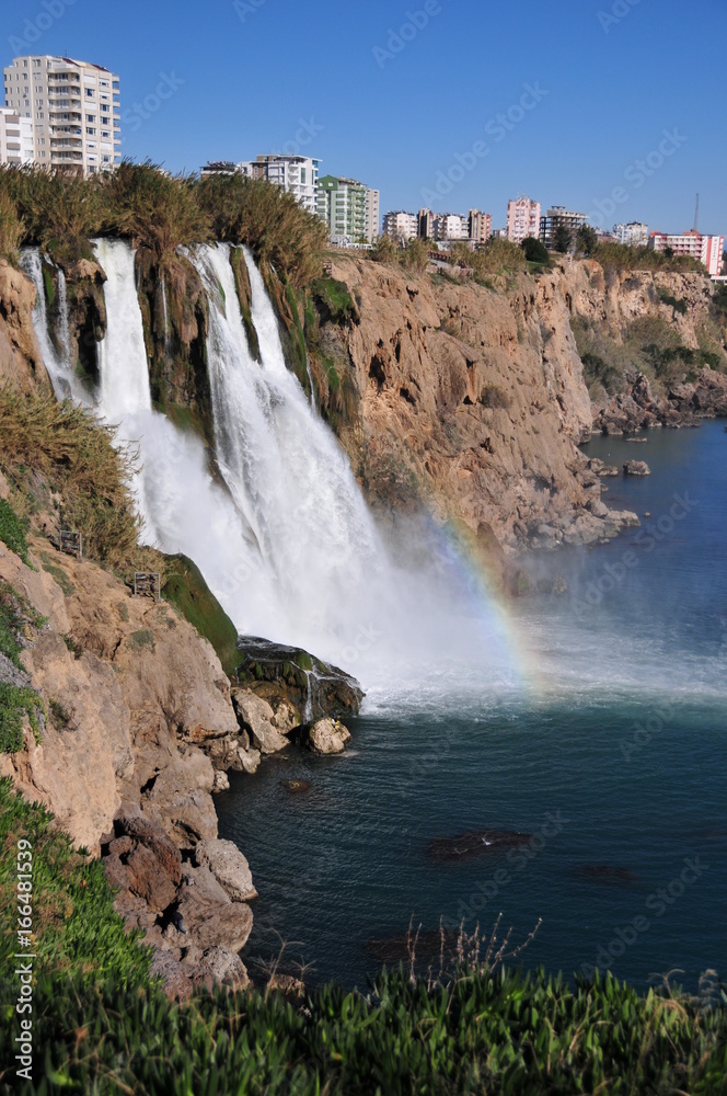 Duden waterfall in Antalya, Lara, with a visible rainbow, Mediterranean sea, rocks, stones and buildings around. Duden waterfall in Antalya, Lara, with a visible rainbow, Mediterranean sea, rocks, stones and buildings around.