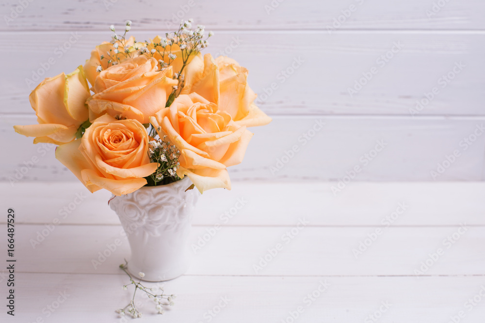 Obraz premium Fresh peach color roses flowers in white vase on wooden background.
