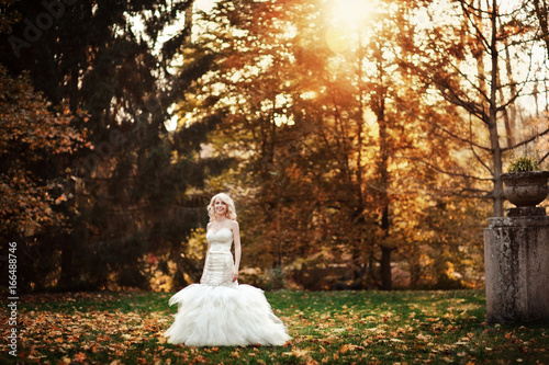 Blonde bride in a white dress in a sunlit park