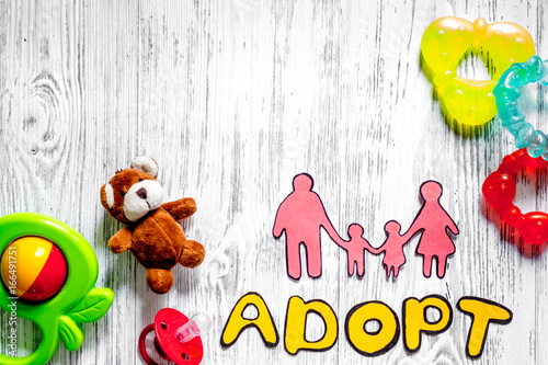 Adopt word, paper silhouette of family and toys on light wooden table background top view copyspace photo