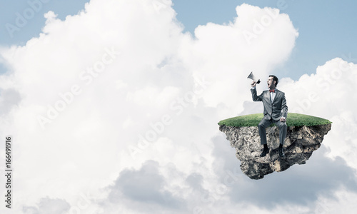 Businessman floating on island in sky and announcing something i © adam121