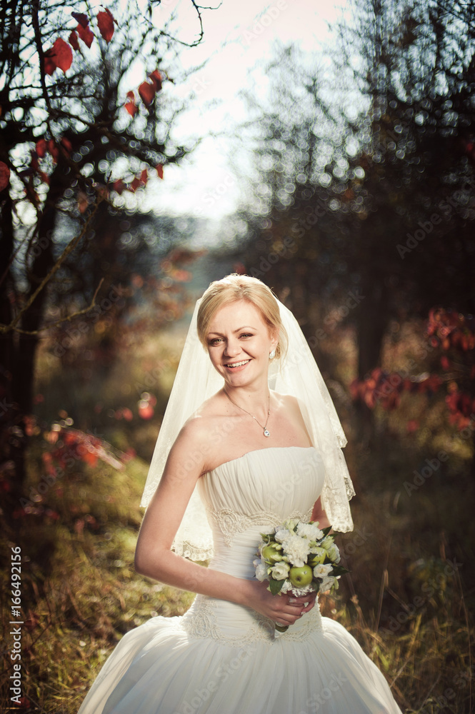 Blonde bride in a white dress in a sunlit park