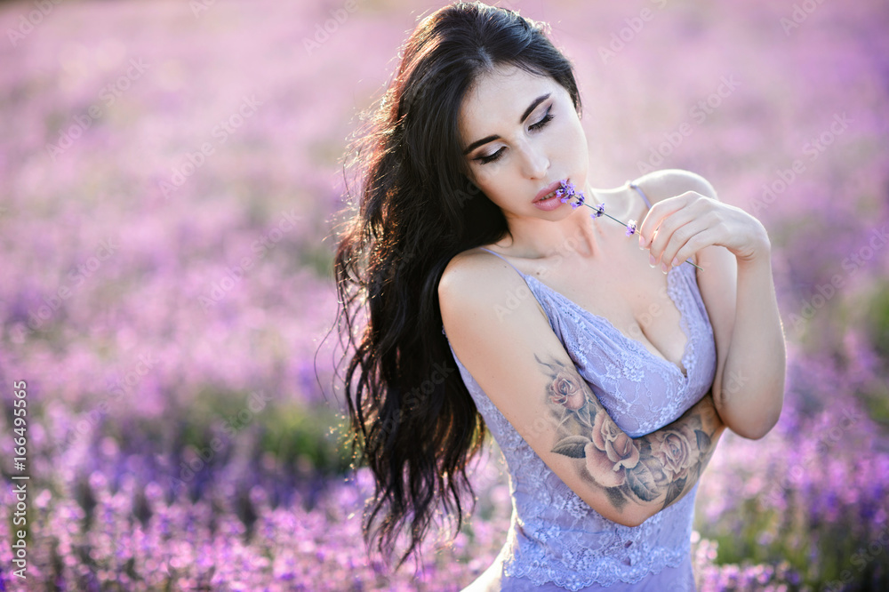 Naklejka premium Beautiful woman in a field of lavender on sunset. Woman in amazing dress walk on the lavender field.