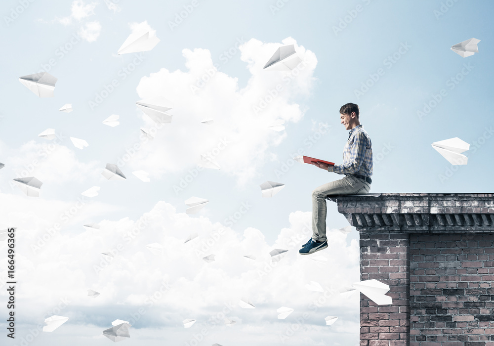 Handsome student guy on roof edge reading book and paper planes Handsome student guy on roof edge reading book and paper planes