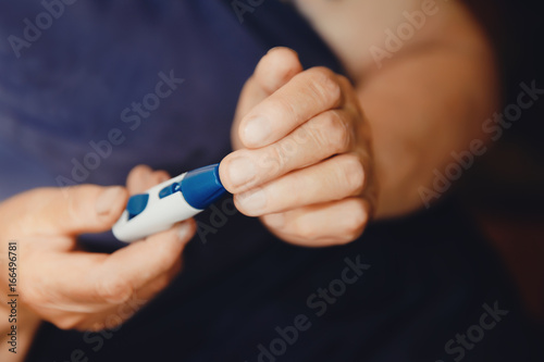 woman aged old fingers with wrinkles measure sugar level with glucometer  pierce finger with needle  concept of risk of diabetes in old women.