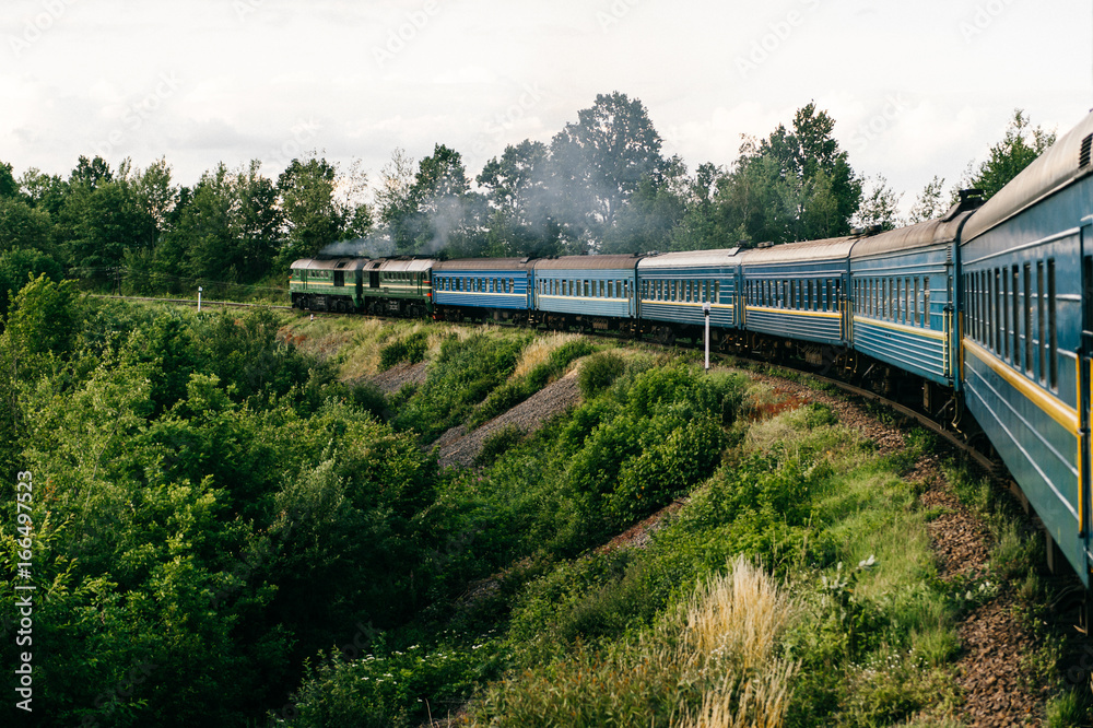Obraz premium Photo of riding train among summer nature. View out of window. Travelling by train. Railroad turn. Going to vacation. Tourism and voyage. Railway outdoor. Vintage locomotive moving with old wagons
