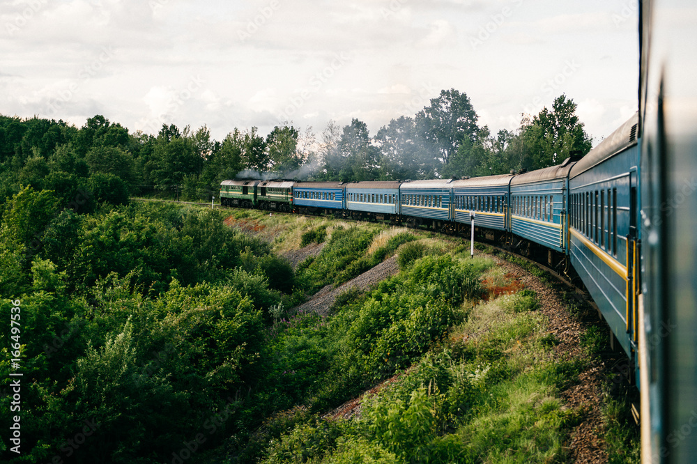 Photo of riding train among summer nature. View out of window. Travelling by train. Railroad turn. Going to vacation. Tourism and voyage. Railway outdoor. Vintage locomotive moving with old wagons Photo of riding train among summer nature. View out of window. Travelling by train. Railroad turn. Going to vacation. Tourism and voyage. Railway outdoor. Vintage locomotive moving with old wagons