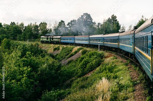 Photo of riding train among summer nature. View out of window. Travelling by train. Railroad turn. Going to vacation. Tourism and voyage. Railway outdoor. Vintage locomotive moving with old wagons