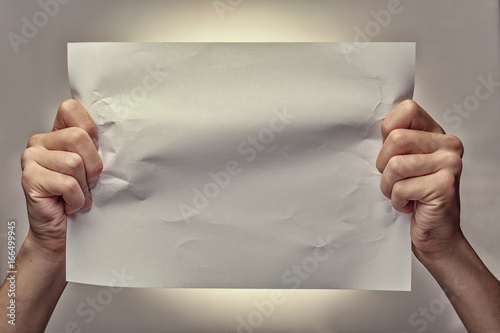 Man hands holding a crumpled blank piece of paper for ad on a gray background