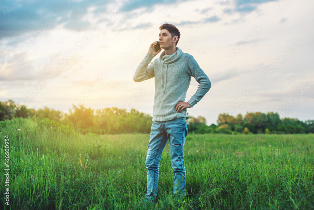 Young man businessman talking at mobile phone outside on a grass field
