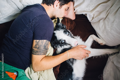 A man playing and cuddling in bed with an Australian Shepherd boarder collie miz photo