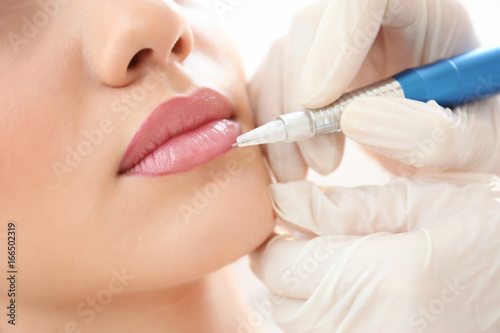 Young woman having permanent makeup on lips in beautician salon