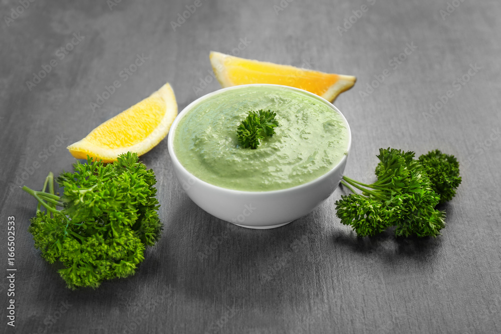 Delicious yogurt sauce in bowl with ingredients on grunge background