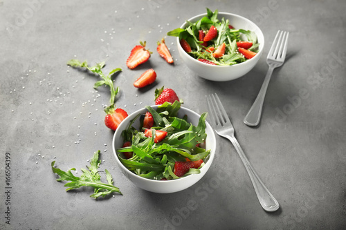 Bowls with tasty strawberry arugula salad on table