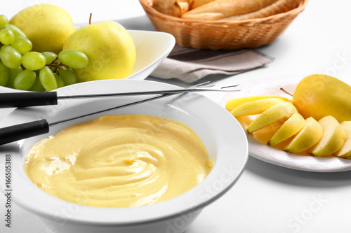 Cheese fondue in plate with slices of apple on white table