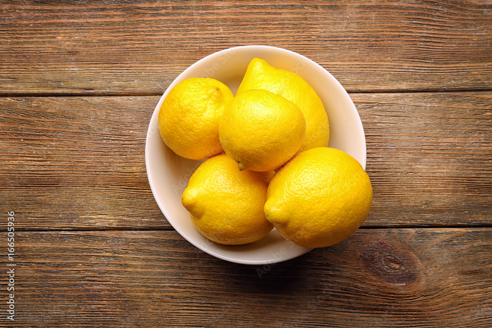 Bowl with delicious lemons on wooden table