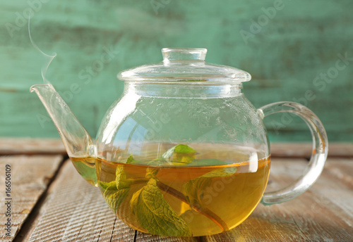 Glass teapot with hot tasty lemon balm tea on wooden table
