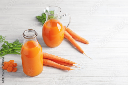 Delicious carrot juice in bottle and jug on wooden table