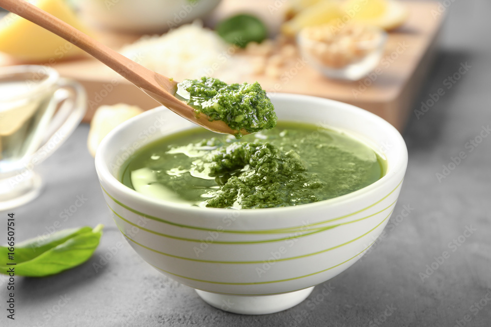 Spoon with delicious sauce over bowl on grey table Spoon with delicious sauce over bowl on grey table