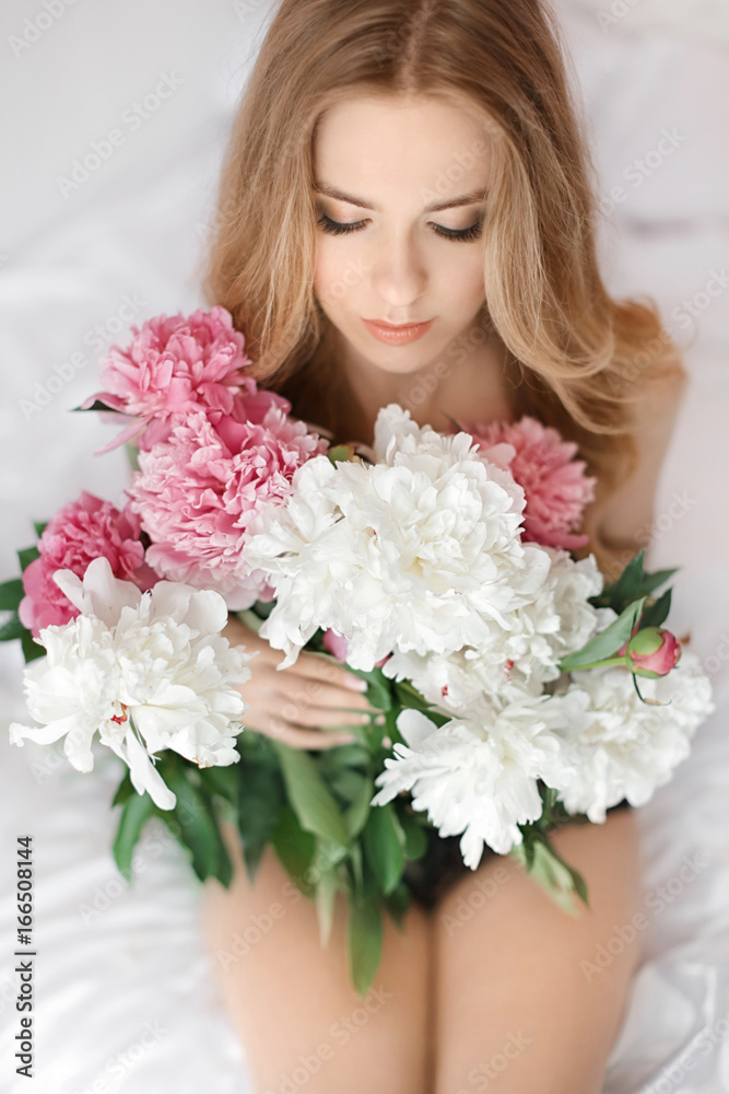 Beautiful young woman with bouquet of peonies on bed at home Beautiful young woman with bouquet of peonies on bed at home