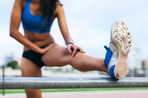Closeup of an african american female sprinter doing stretching exercices on an athletics track.