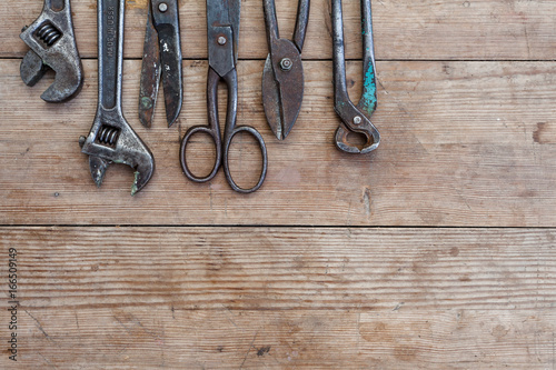 Viiew of vintage rusted tools on old wooden table: pliers, pipe wrench, screwdriver, hammer, metal shears, saws and other photo