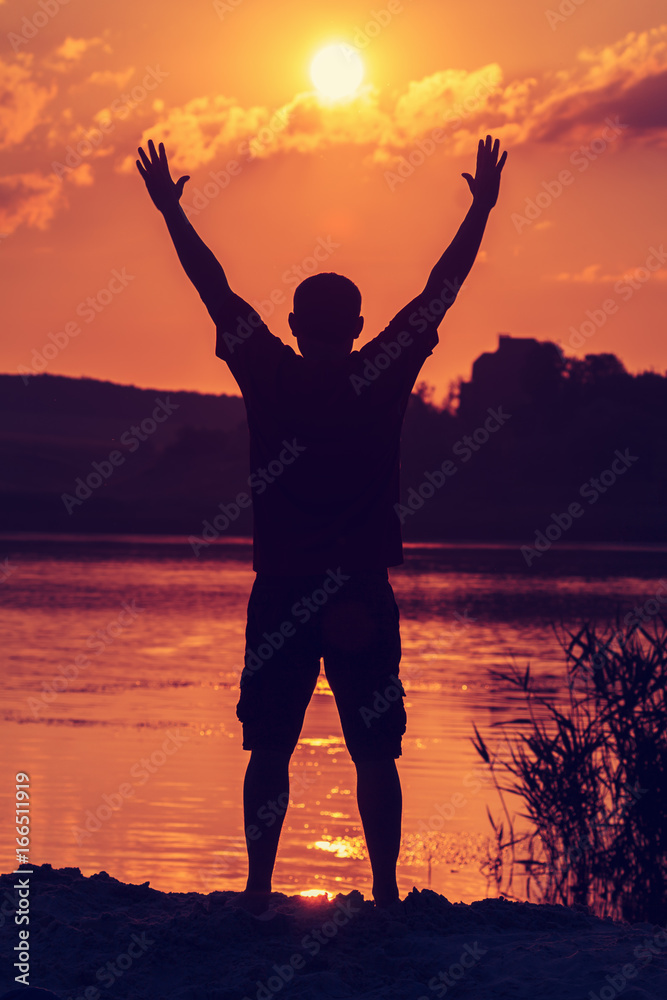 Fototapeta premium Man with his hands up at the sunset on the beach