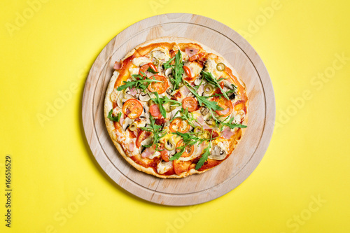 Pizza on wooden board on yellow background, top view