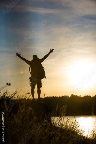A young tourist stands on a rock with his hands up, enjoying nature. Beautiful landscape.