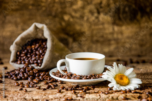 Coffee. A hot cup of coffee and roasted coffee beans on a wooden table. Dark background