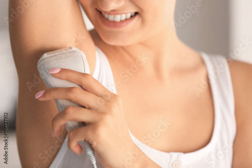 Beautiful young woman epilating armpits at home, closeup