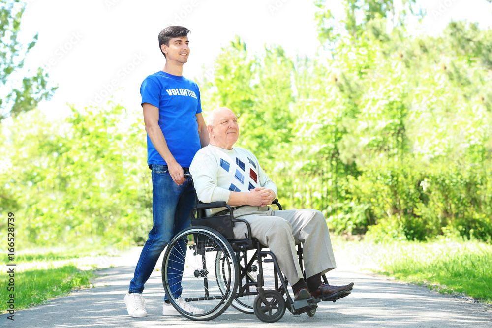 Happy senior man on wheelchair with young male volunteer outdoors Happy senior man on wheelchair with young male volunteer outdoors
