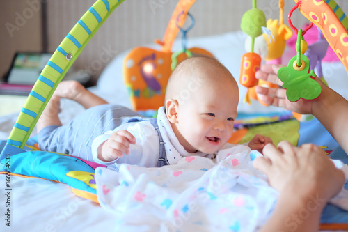 Cute little Asian 5 - 6 months old  baby boy child at tummy time on the play gym playing with his Daddy on Bed in Bedroom at Home
