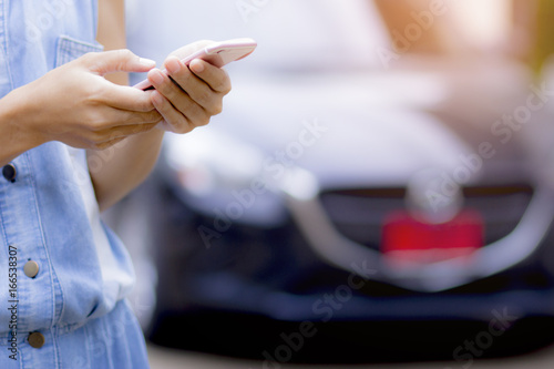 This image is a picture of a woman using a cell phone with a new car in the back. The concept is technology and money.