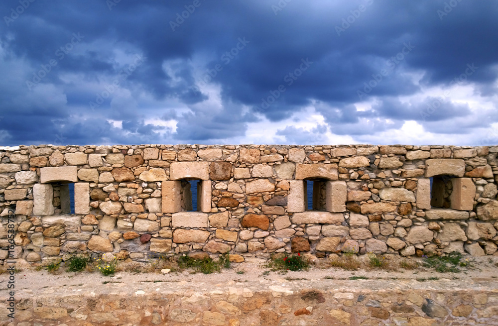 Beautiful old beige stone wall on the background of bright blue sky in Rethymnon, Crete
