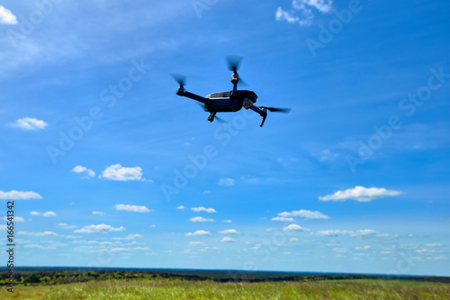 Flight of a gray quadrocopter against a blue sky.