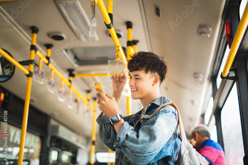 фотографія Asian man taking public transport, standing inside bus.